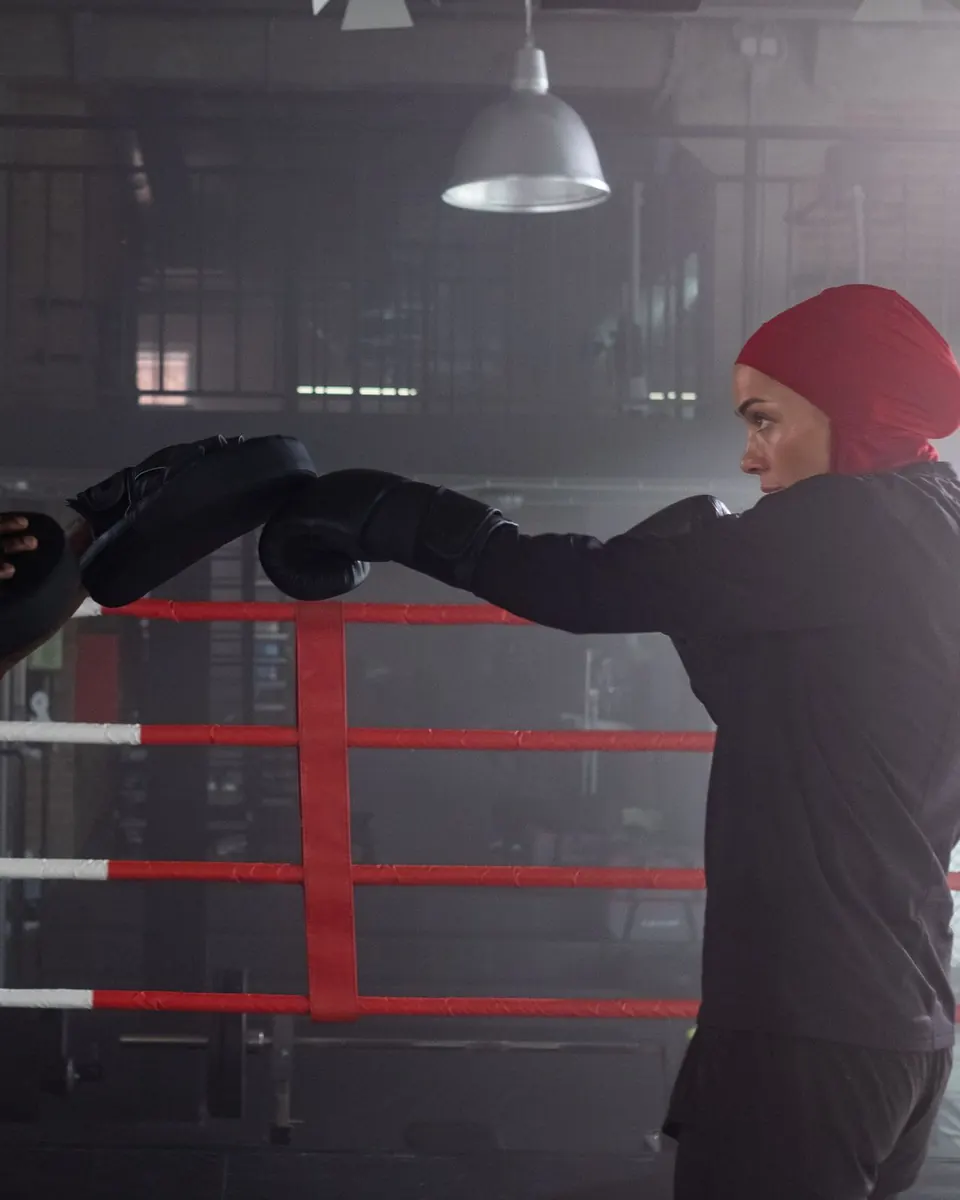 A woman throwing a punch into a coach's pads in a boxing gym
