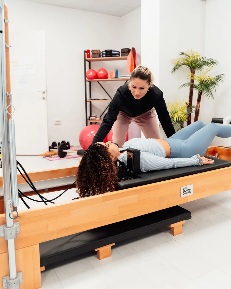 An instructor guiding a client through an exercise on a wooden reformer