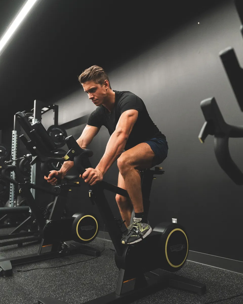 A rider out of the saddle on a studio bike in a dark gym