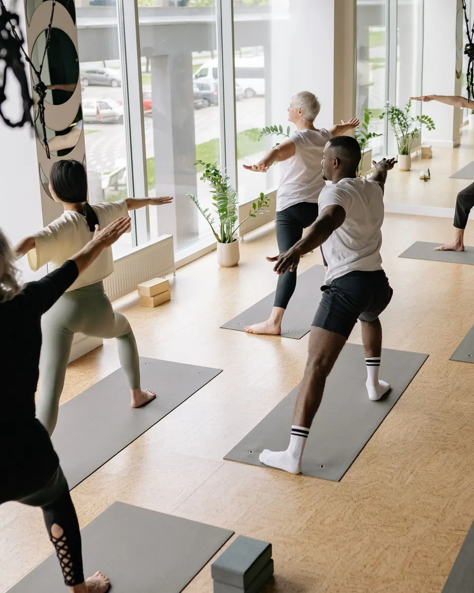 A mixed yoga class holding a standing pose in a bright studio